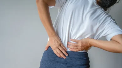 Mulher com dor lombar, colocando as mãos nas costas em sinal de desconforto.