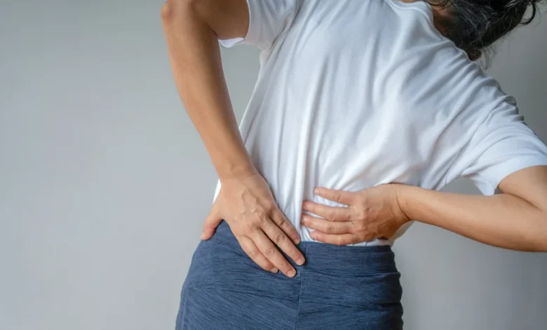 Mulher com dor lombar, colocando as mãos nas costas em sinal de desconforto.