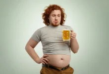 Homem segurando um copo de chopp, com foco na barriga.