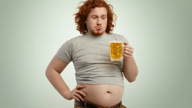 Homem segurando um copo de chopp, com foco na barriga.
