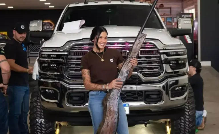 Ana Castela segurando luminária em formato de espingarda ao lado de empresários.
