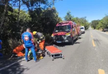 Carro acidentado em ribanceira com equipes de resgate ao redor.