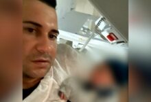 Pai com bebê recém-nascido nos braços em frente a um elevador.
