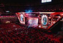 Palco iluminado com artistas sertanejos se apresentando.