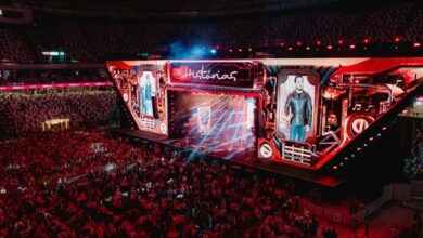 Palco iluminado com artistas sertanejos se apresentando.