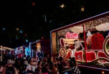 Caminhões decorados da Caravana de Natal da Coca-Cola iluminando a noite.