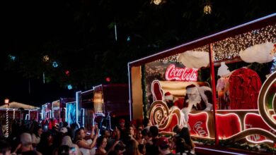 Caminhões decorados da Caravana de Natal da Coca-Cola iluminando a noite.