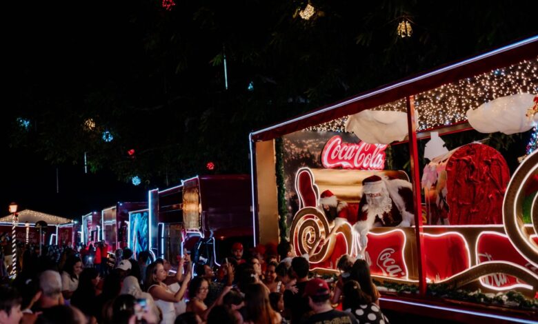 Caminhões decorados da Caravana de Natal da Coca-Cola iluminando a noite.